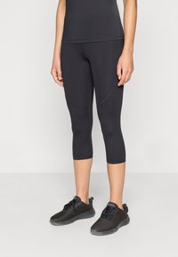 Μαύρα κάπρι κολάν από ελαστικό ύφασμα, με εφαρμοστή γραμμή και ραφές ως διακόσμηση, συνδυασμένα με μαύρα αθλητικά παπούτσια.