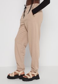 Beige Jogginghosen mit einem Kordelzugbund, seitlichen Taschen und einer entspannten Passform, kombiniert mit klobigen beigen Sandalen mit einem Riemenverschlusssystem.