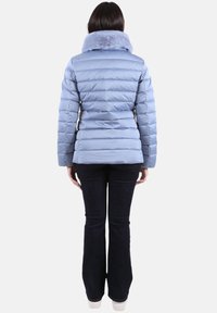 Chaqueta acolchada azul claro con cuello de piel sintética, textura acolchada vertical y silueta ajustada, combinada con vaqueros oscuros de pata acampanada.