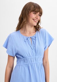 Light blue, short-sleeve dress made of textured fabric. Features a round neckline with a keyhole and tie detail, cinched waist design.