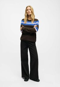 Brown knit sweater with blue and pink stripes, paired with black wide-leg pants and black shoes. Textured fabric with loose fit.