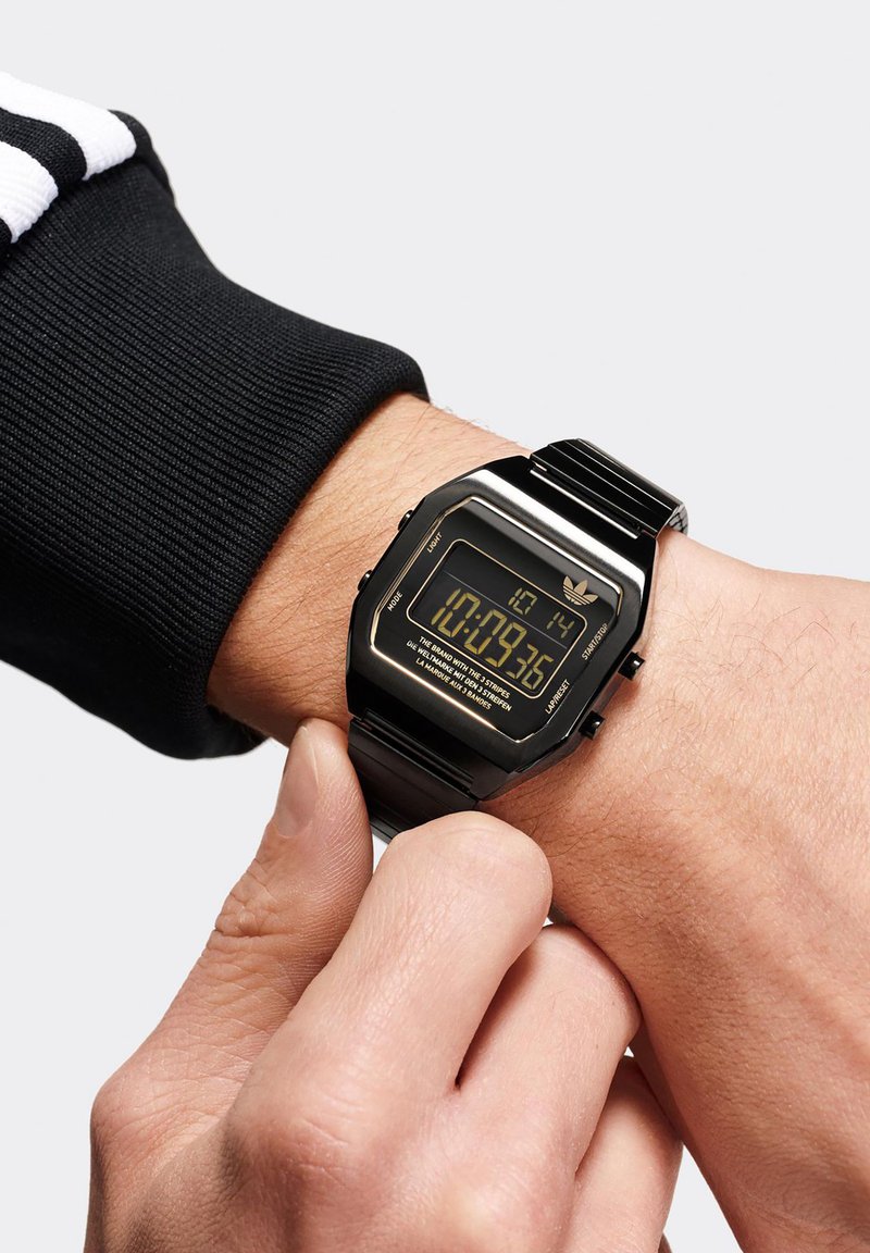 Digitale Armbanduhr mit schwarzem Metallgehäuse und -armband, ausgestattet mit einem rechteckigen LCD-Display. Das Display zeigt die Zeit im digitalen Format an.