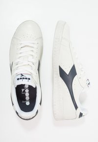 Sneakers in pelle bianca con accenti blu navy, lati perforati e suole in gomma piatta. Caratterizzati da lacci bianchi e un'etichetta con logo sulla linguetta.