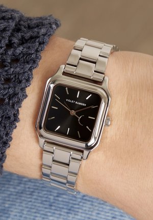 Montre en acier inoxydable argenté avec un cadran noir carré, des index argentés et une fonction date. Bracelet de style chaîne avec des maillons polis.
