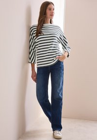 Pruhovaný svetr v bílé a tmavě modré barvě, s třetinovými rukávy, kombinovaný s modrými džíny a bílými teniskami.