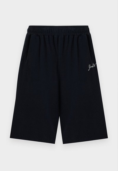 Μαύρες σορτς μέχρι το γόνατο με ελαστική μέση και μικρό λευκό κείμενο σε πλάγια γραφή στη δεξιά πλευρά.