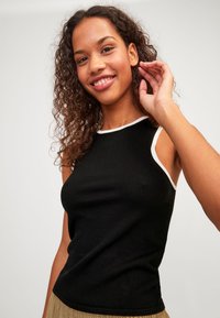 Top negro sin mangas con un escote blanco, textura acanalada, diseño ajustado y hombros al aire, combinado con una falda de color neutro.