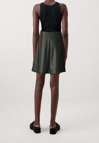 Gonna in pelle verde con una forma svasata, dotata di chiusura con zip sul retro. Abbinata a un top smanicato nero e sandali con plateau neri.