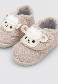Zapatillas de casa beige y peludas con un tejido texturizado, que presentan un diseño de cara de oveja en la parte delantera, puntera redondeada y una suela de goma flexible.