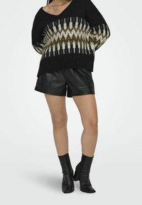 Schwarzer Strickpulli mit einem geometrischen Muster in Creme und Oliv, kombiniert mit hochgeschnittenen schwarzen Leder-Shorts und schwarzen Knöchelschuhen.