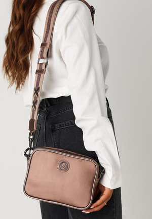 Brązowa torebka crossbody z ekoskóry o gładkiej fakturze, z zamknięciem na zamek błyskawiczny i wzorzystym regulowanym paskiem. Szczegół z logo z przodu.