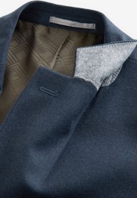 Sötétkék gyapjúkabát gallérja és felső része, szürke filc aljeggyel és mintás béléssel.