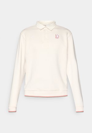 Langermet kremfarget polo-skjorte med tre knapper, røde og svarte stripete mansjetter og nederkant, Nike-logo på høyre bryst og rødt løveemblem på venstre bryst.