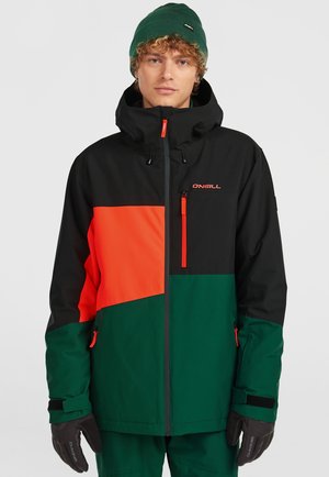 Kleurige skijas met een zwart, groen en oranje kleurblokontwerp, voorzien van ritszakken en een verstelbare capuchon, vervaardigd uit duurzaam materiaal.