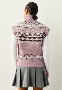 Mouwloos, gebreid vest in pastelroze met Fair Isle-patronen in wit en bruin. Voorzien van een hoge kraag en een ontwerp tot op de heup.