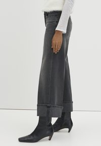 Jeans a vita alta e gamba larga in denim grigio scuro con orlo risvoltato, abbinati a stivaletti neri con punta appuntita.