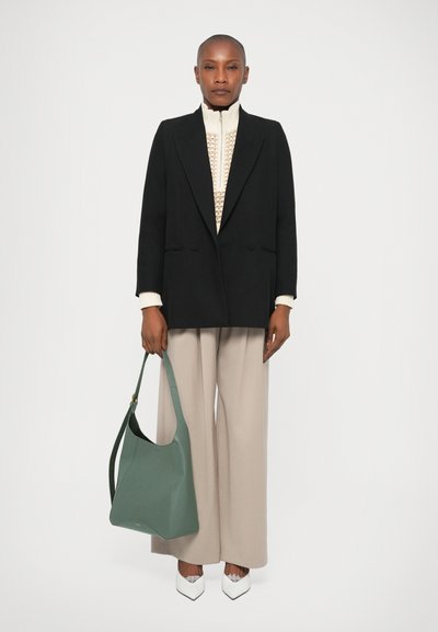 Blazer negru cu două rânduri de nasturi, pulover din tricot crem, pantaloni largi bej, geantă de umăr din piele verde și pantofi albi cu vârful ascuțit.