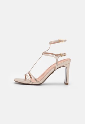 Gold metallic high-heeled sandal with a strappy design, open toe, and ankle buckle. Features a textured insole and smooth surface.