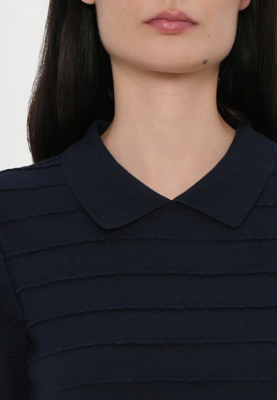 Top tricotat bleumarin cu guler rotund și dungi orizontale texturate cu margini ondulate, subliniind un design curat și structurat.