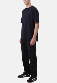 Svart bomullströja med avslappnad passform, kombinerad med svarta cargobyxor med sidofickor och svarta sneakers med vita ränder.
