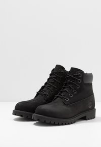 Stivali alla caviglia in suede nero con suola in gomma, dotati di lacci neri a contrasto, occhielli in metallo e logo impresso sul lato.