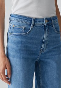 Jeans in denim azzurro chiaro a vita alta, con taglio dritto, dotati di cinque tasche, chiusura con zip e dettagli di cucitura color rame.