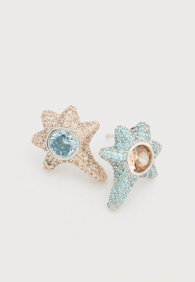 Σκουλαρίκια σε σχήμα αστεριού με υφή φινιρίσματος. Το ένα σε ανοιχτό χρυσό με μία μπλε πέτρα, το άλλο σε ανοιχτό μπλε με μία καφέ πέτρα.
