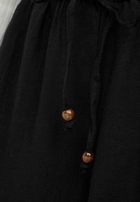 Tissu noir avec deux cordons noués, chacun se terminant par une petite perle en bois marron.