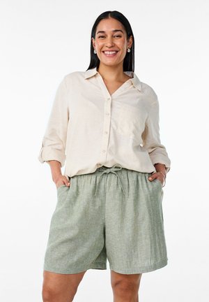 Light beige button-up shirt with rolled sleeves, paired with relaxed green linen shorts featuring an elastic waistband and side pockets.