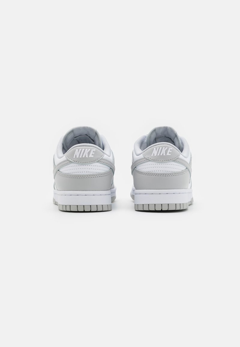 Baskets Nike en cuir blanc avec accents gris, col rembourré et semelle texturée. Présente le logo "Nike" sur le talon et sur le côté.