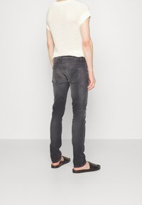 Jeans ajustados de color gris oscuro con cintura de altura media, diseño de cinco bolsillos y costuras en contraste, combinados con un top de punto beige texturizado y sandalias negras de tiras.