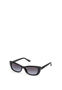 Gafas de sol negras con un marco grueso y brillante. Forma de ojo de gato, lentes oscuros con degradado y logotipo grabado en la patilla. Diseño elegante y textura suave.