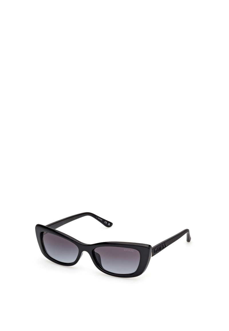 Gafas de sol negras con un marco grueso y brillante. Forma de ojo de gato, lentes oscuros con degradado y logotipo grabado en la patilla. Diseño elegante y textura suave.