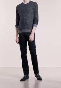 Pull gris foncé texturé avec un motif géométrique, associé à un pantalon noir slim et des bottines noires. Encolure ronde simple.