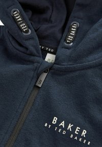 Sudadera con cremallera en color azul marino, hecha de una tela suave, con una cremallera de contraste y un tirador en forma de "B", y logotipos bordados en la capucha y en la parte frontal.