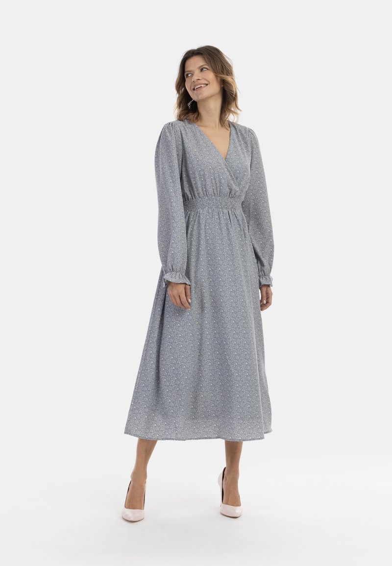 Lichtblauwe bloemenmaxi-jurk met lange pofmouwen, een diepe V-hals en gerimpelde taille, gecombineerd met blush hakken.