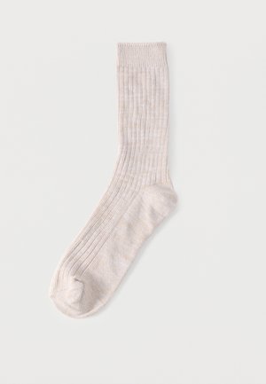 Calcetín de canalé beige claro para hombre, extendido plano, mostrando la suela acolchada y el puño elástico sobre un fondo blanco liso.