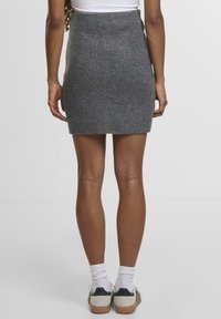 Grå ribstrikket miniskørt med en tætsiddende talje, lige silhuet og blød tekstur, parret med hvide sokker og afslappede sko.