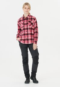 Rot-schwarzes Karo-Hemd mit Knöpfen und zwei Brusttaschen, kombiniert mit schwarzen, taillierten Outdoor-Hosen und schwarzen Schnürstiefeln.
