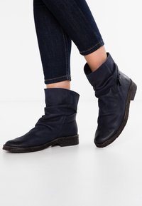 Botas de tobillo de cuero azul marino con un diseño holgado, punta redondeada y suela de goma texturizada. Presentan detalles decorativos de hardware.