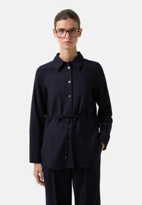 Navy blouse met een kraag, lange mouwen, knopen aan de voorkant, elastische tailleband en zijzakken in een gladde, lichte stof.