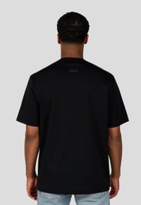 Czarny t-shirt z krótkim rękawem i okrągłym dekoltem, wykonany z gładkiego materiału, z subtelną metką marki z tyłu.