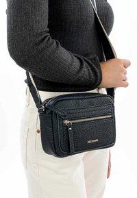 Dámská crossbody taška z černé strukturované kůže se zlatými zipovými detaily, obdélníkový tvar, nastavitelný popruh a přední kapsa na zip.