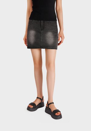 Donna che indossa una minigonna di jeans nera sbiadita, un top nero senza maniche e sandali con zeppa neri con cinturini intrecciati.