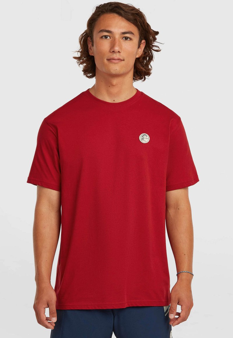 Rotes Baumwoll-T-Shirt mit Rundhalsausschnitt, kurzen Ärmeln und einem runden Logopatch auf der linken Brust. Glatte Textur, reguläre Passform.