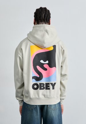 Hellgraue Kapuzenjacke mit einem großen Grafikdesign auf dem Rücken, das abstrakte Formen in Pink, Gelb, Blau und Schwarz zeigt. Schwarzer "OBEY"-Text.
