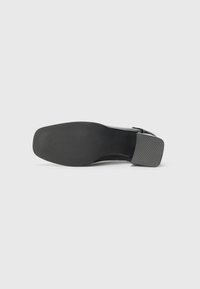 Black high-heeled shoe with a smooth leather upper and a square textured heel. The sole features horizontal grip lines for traction.