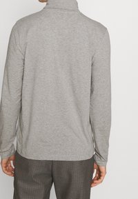 Graues langärmliges Poloshirt mit hohem Kragen und strukturiertem Stoff; die Rückansicht zeigt eine glatte Verarbeitung und eine bequeme Passform.