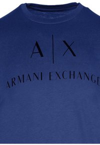 T-shirt in cotone blu navy con la scritta "A|X ARMANI EXCHANGE" in nero, visualizzata in modo prominente sul davanti con caratteri di dimensioni variabili.