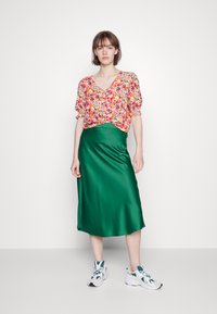 Top floral de mangas curtas com mangas franzidas, combinado com uma saia brilhante de cetim verde e ténis brancos com detalhes em teal.